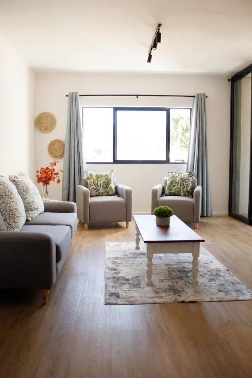Bright living room with gray armchairs, woven wall art, and garden views