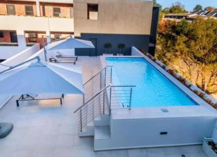 Modern rectangular swimming pool on rooftop deck with loungers and railings