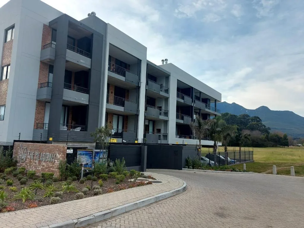 Modern multi-story apartment building with mountain backdrop and landscaped grounds