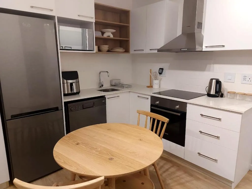 Modern kitchen with white cabinetry, stainless steel appliances, and wooden dining table