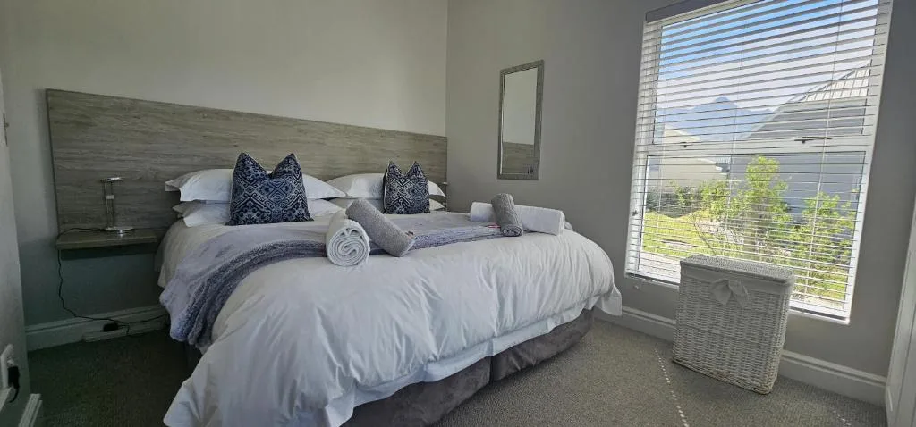 Bright bedroom with queen bed, decorative pillows, and large windows overlooking gardens