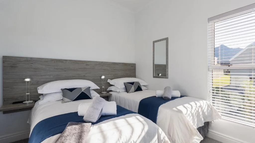 Modern bedroom with twin beds, dark headboard, white linens, blue accents