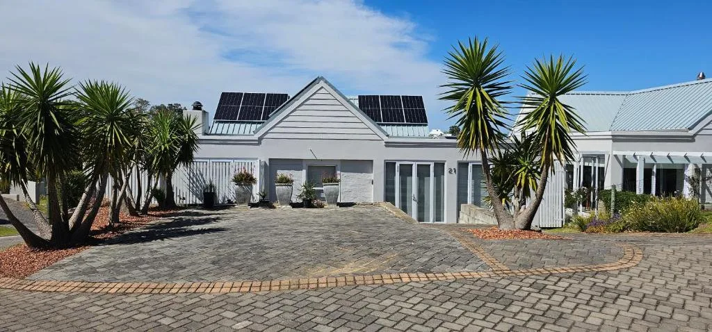 Modern white cottage with solar panels and manicured driveway entrance