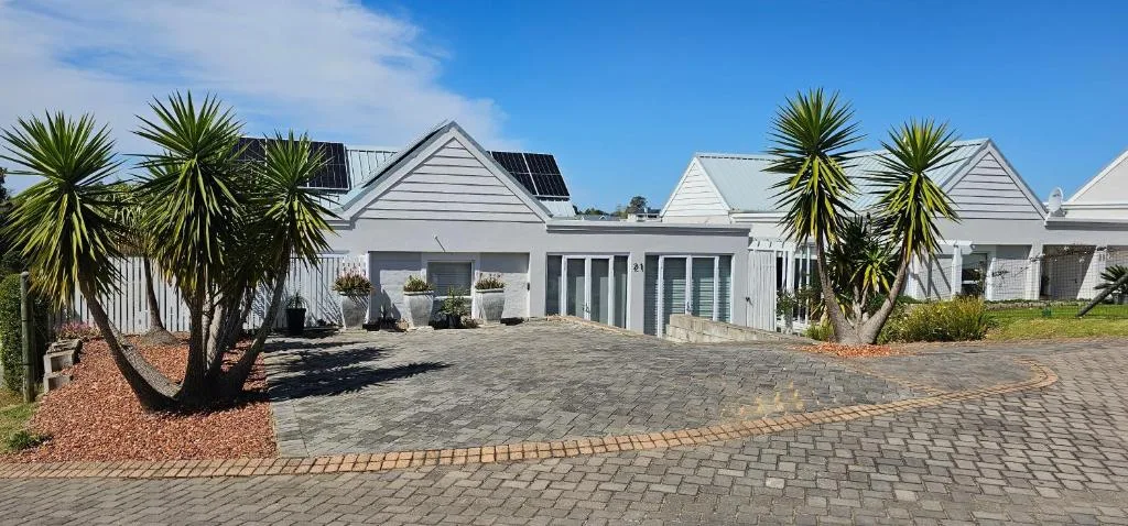 Modern white cottage with paved driveway, palm trees, and manicured gardens