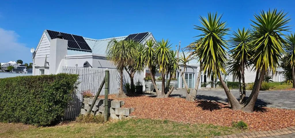 White house with solar panels, palm trees, and manicured garden entrance