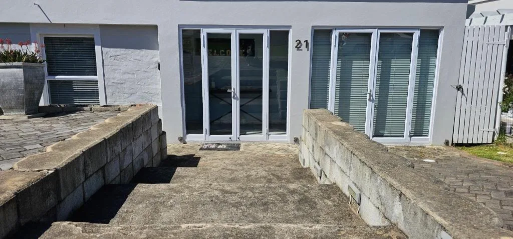 Modern white apartment building with blue-trimmed doors and windows, paved courtyard entrance