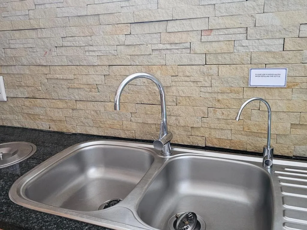 Double stainless steel sink with chrome faucets and stone tile backsplash