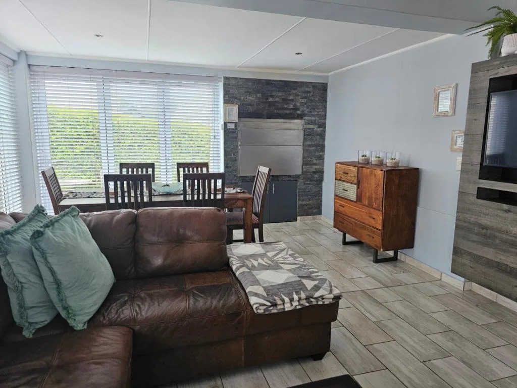 Modern lounge with brown leather sofa, dining table, and large windows overlooking garden