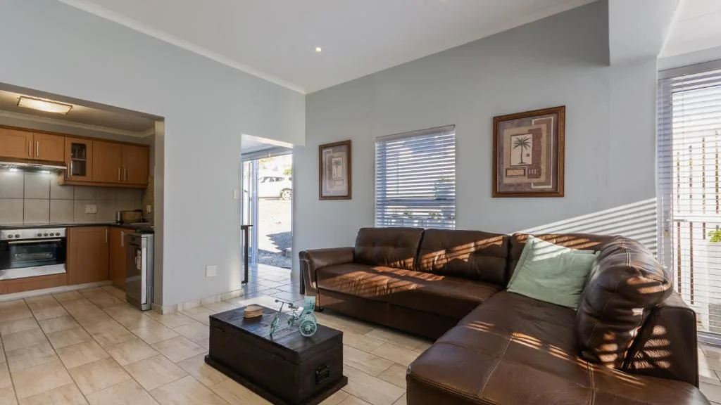 Open-plan lounge with brown leather sofa and kitchen visible through archway