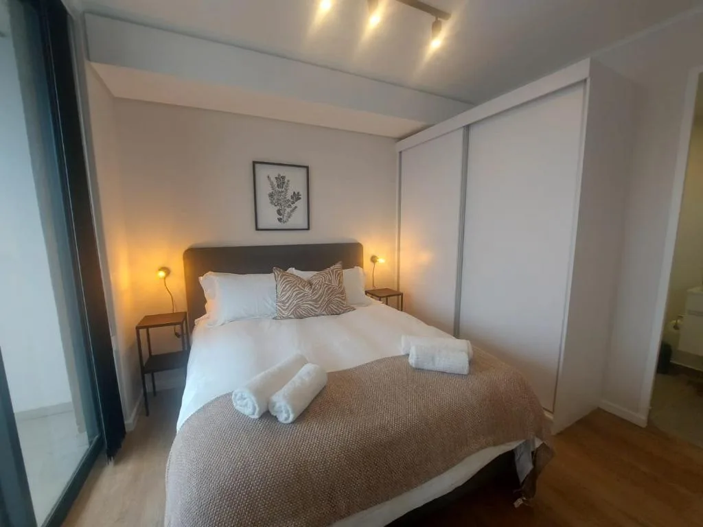 Modern bedroom with queen bed, white linens, bedside lamps, and built-in wardrobe