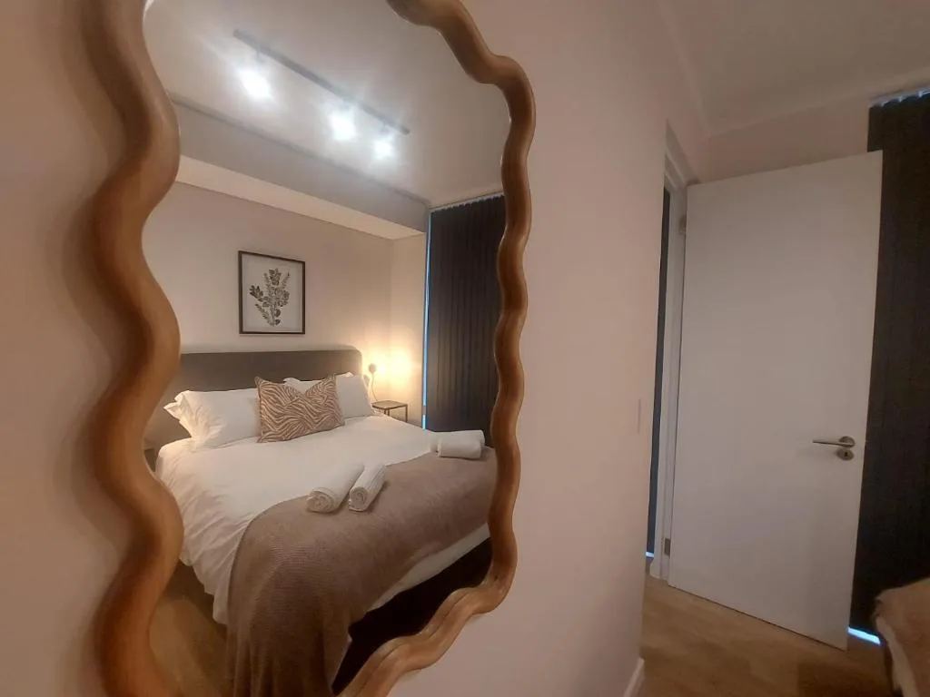 Modern bedroom with queen bed, wavy mirror, and soft warm lighting