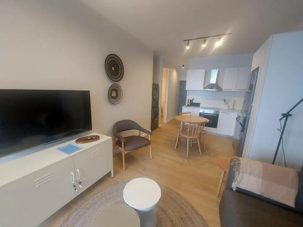 Modern open-plan lounge with TV, dining area, and kitchen visible