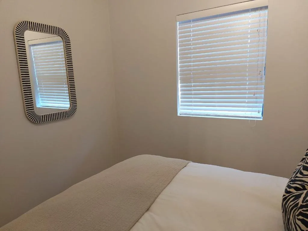 Bright bedroom with double bed, decorative mirror, and window blinds