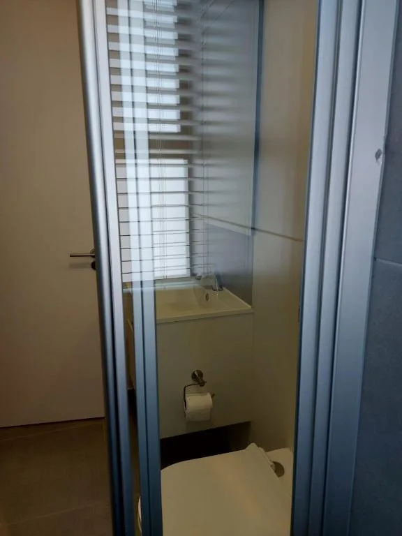 Compact bathroom with toilet, sink, and shower enclosure with striped glass