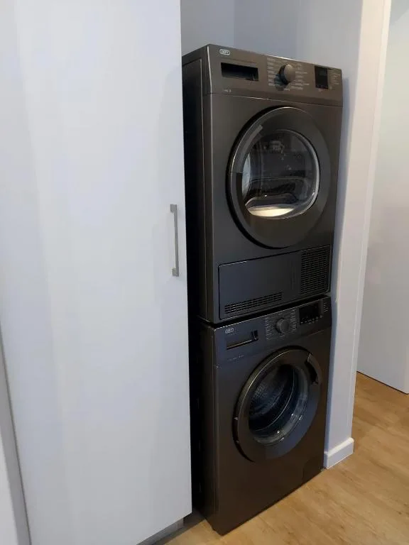 Stacked black washer and dryer in laundry area with white walls