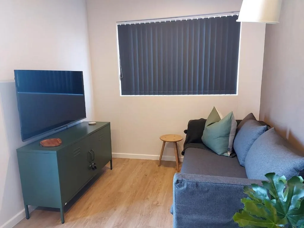 Cozy lounge with sofa, TV, wooden flooring, and natural light from windows