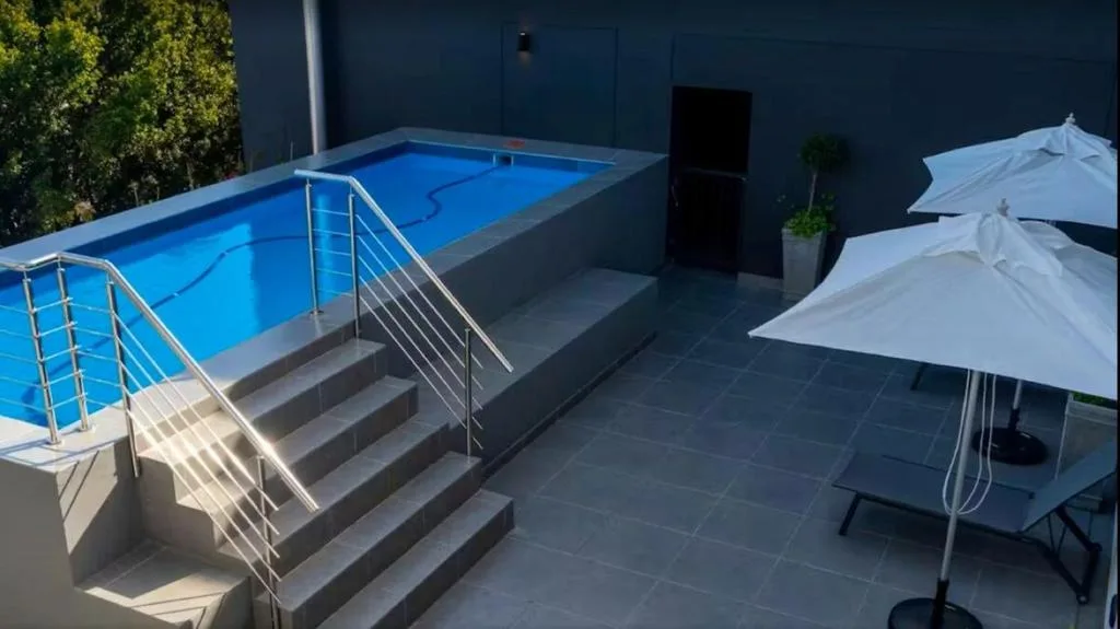 Rectangular swimming pool with metal railing and shaded seating area nearby