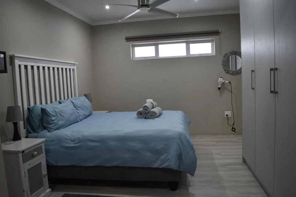 Modern bedroom with queen bed, blue bedding, and en-suite bathroom visible