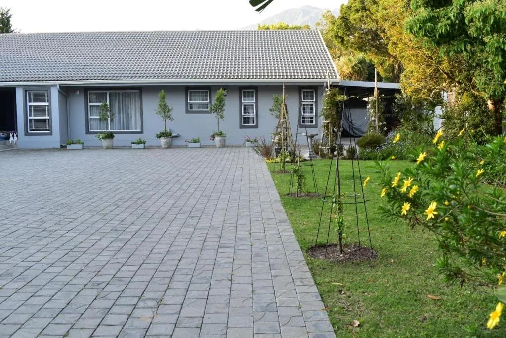 White cottage with paved driveway, potted plants, and manicured garden