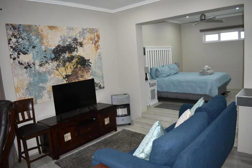 Open-plan lounge with blue sofa, TV stand, and bedroom visible beyond