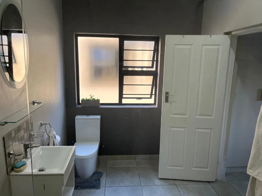 Modern bathroom with sink, toilet, mirror, and window overlooking garden