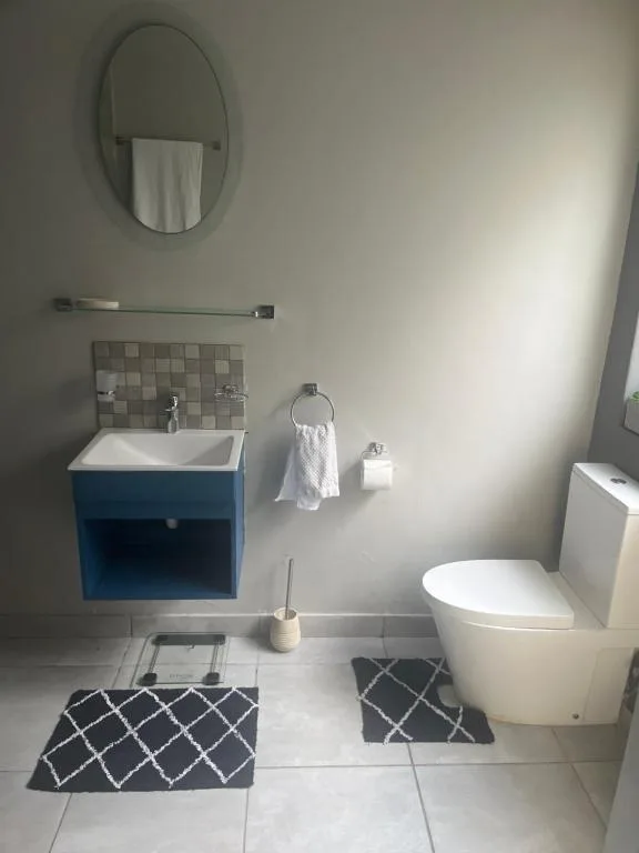 Modern bathroom with blue vanity, oval mirror, toilet, and tiled flooring