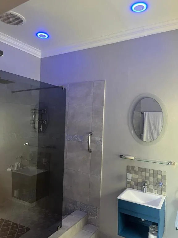 Modern bathroom with walk-in shower, round mirror, blue vanity, ambient lighting