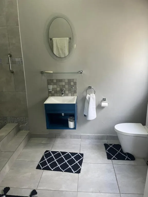 Modern bathroom with blue vanity, oval mirror, and tiled shower area