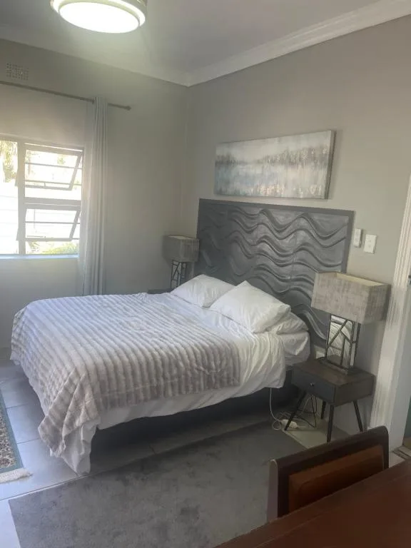Neat bedroom with queen bed, dark headboard, and natural light from window