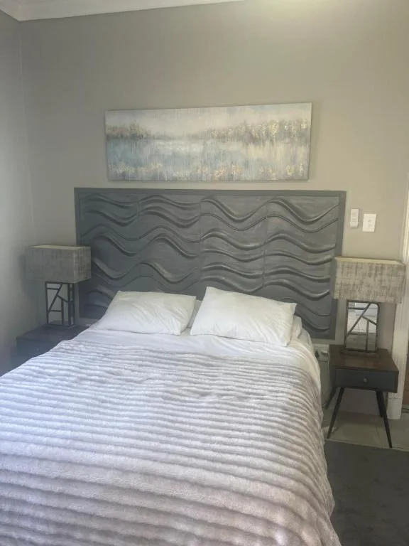 Modern bedroom with textured grey headboard and white pillows, bedside tables with lamps