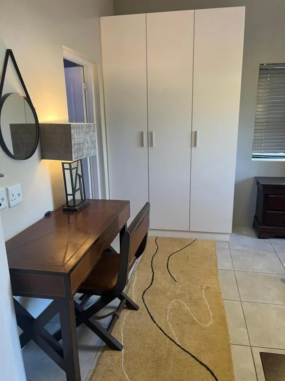 Modern bedroom with wooden desk, round mirror, and white built-in wardrobe