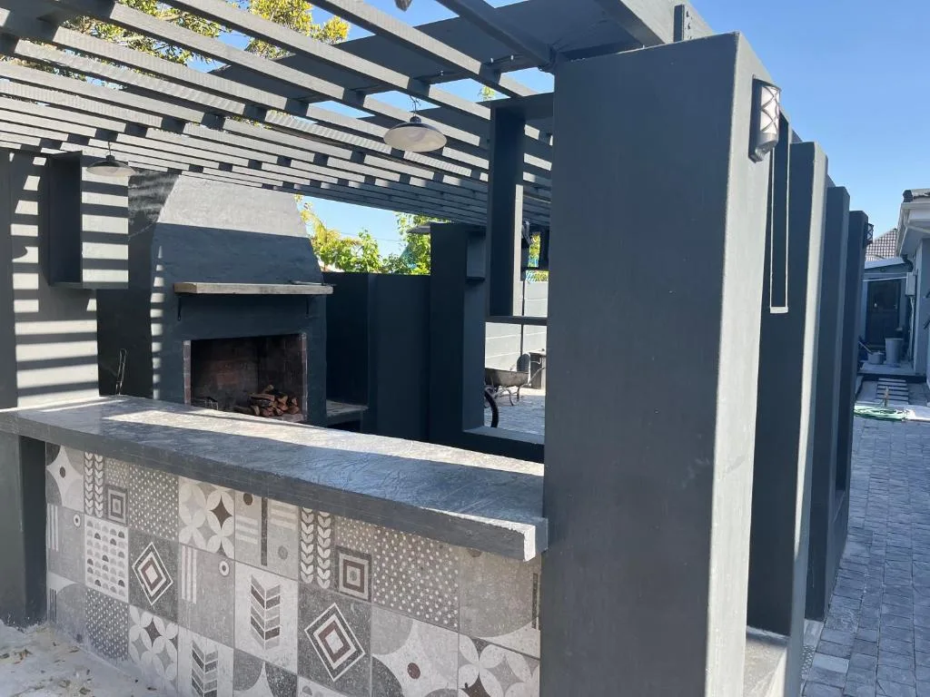 Modern outdoor braai area with pergola and fireplace under clear sky
