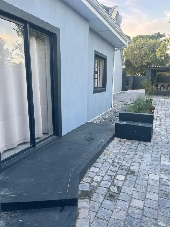 Modern white-walled building exterior with black-framed glass doors and paved courtyard