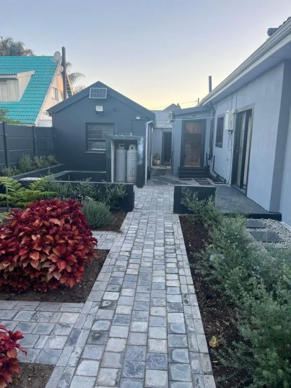 Modern cottage exterior with paved pathway, dark facade, and manicured gardens