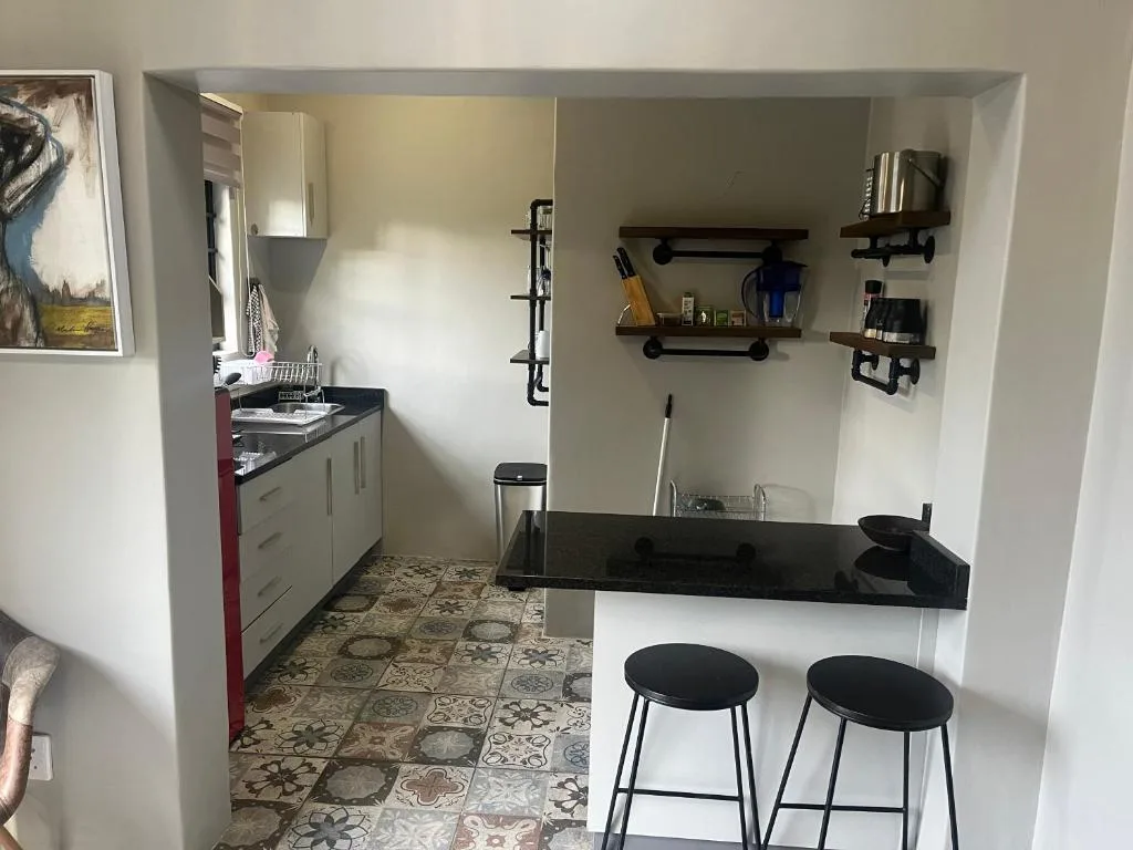 Modern kitchenette with black countertop, bar seating, and open shelving