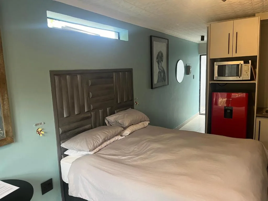 Modern bedroom with queen bed, wooden headboard, and kitchenette visible