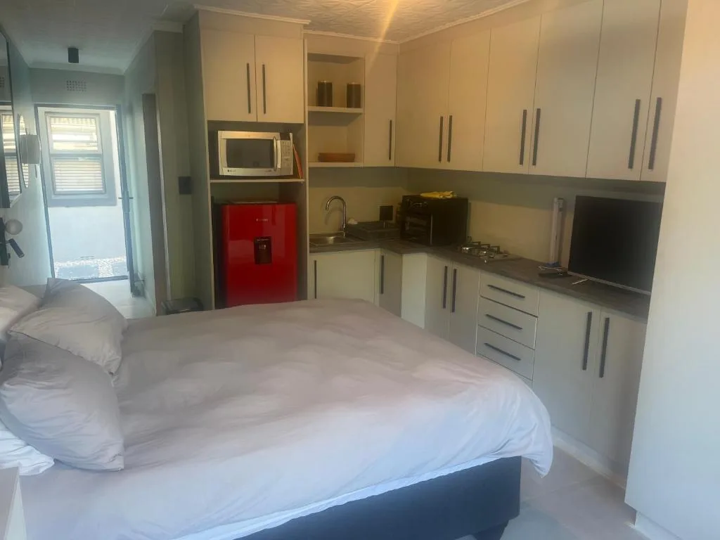 Studio bedroom with integrated kitchen, red fridge, and modern cabinetry