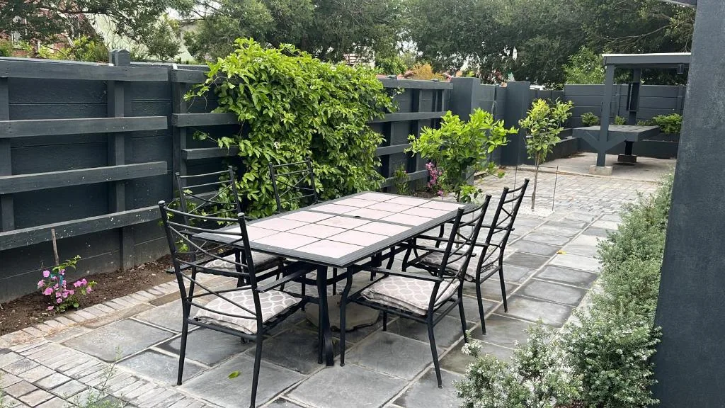 Outdoor patio with dining table and chairs surrounded by greenery