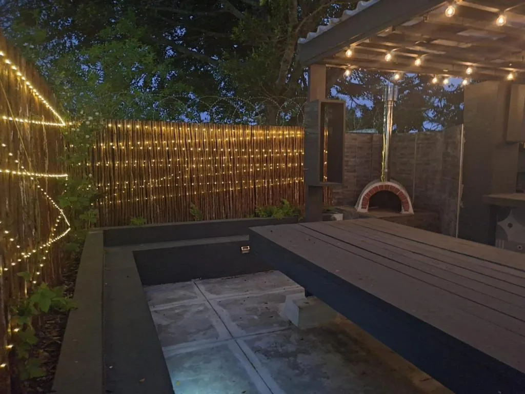 Illuminated outdoor deck with wooden table, pizza oven, and ambient lighting at dusk