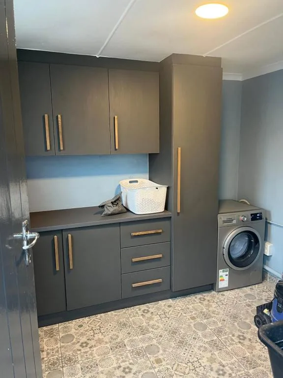Modern laundry room with dark cabinetry, washing machine, and storage solutions