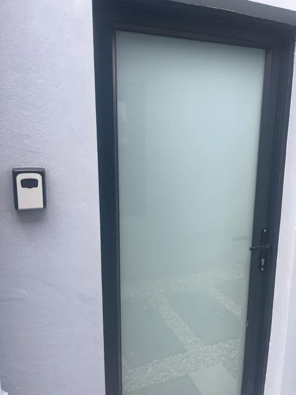 Modern black-framed glass door entrance with keypad lock on white wall
