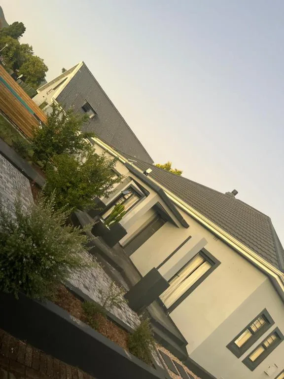 Modern cream and grey residential building facade with pitched roof and surrounding vegetation