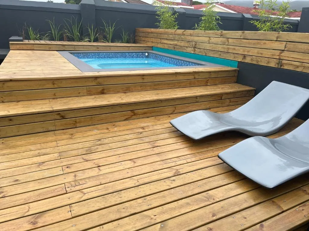 Modern wooden deck with blue swimming pool and white lounge chairs