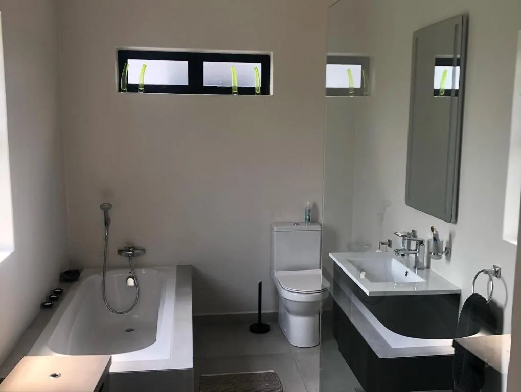 Modern bathroom with bathtub, toilet, double vanity sink, and mirrors