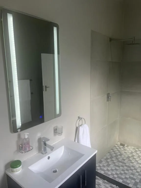 Modern bathroom with illuminated mirror, white sink, and glass shower enclosure