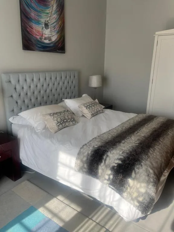 Bright bedroom with upholstered headboard, white linens, and striped throw