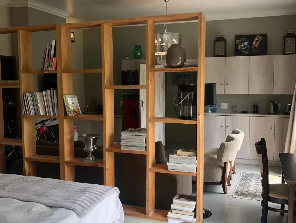 Bedroom with bed, wooden shelving unit, and open-plan living area beyond