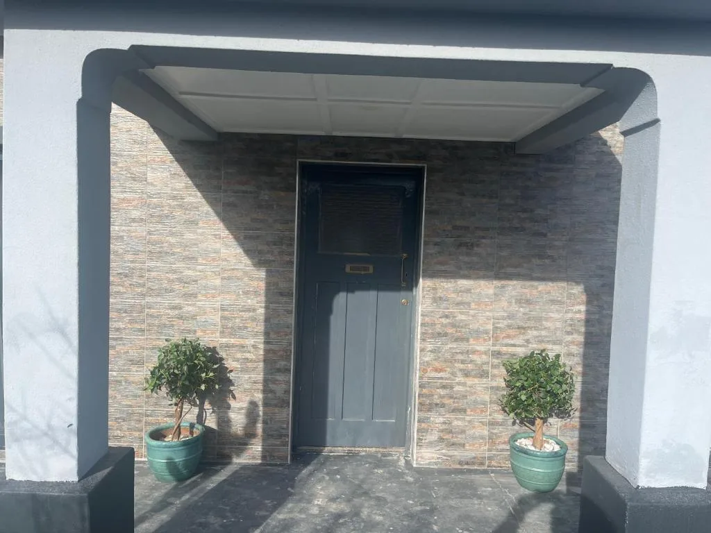 Modern brick entrance with dark door and retractable awning, potted plants flanking