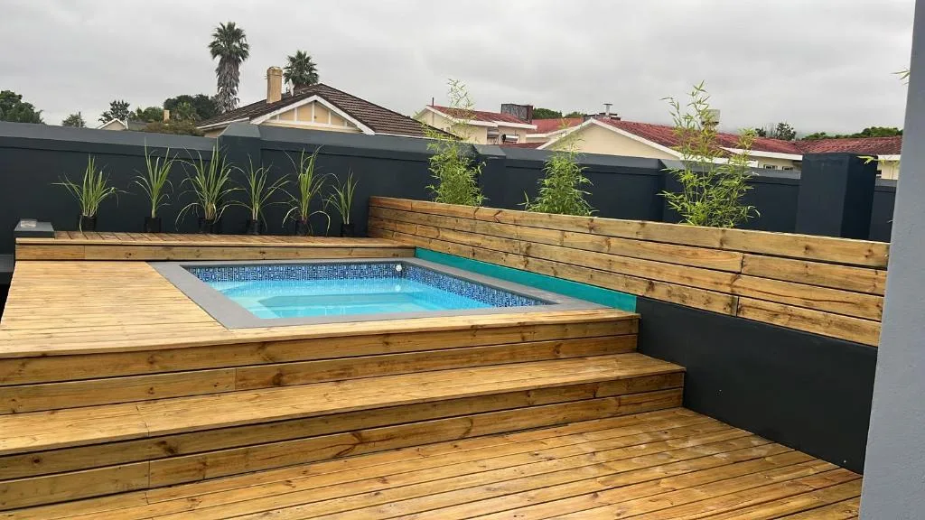 Modern backyard swimming pool with wooden deck and black boundary fencing