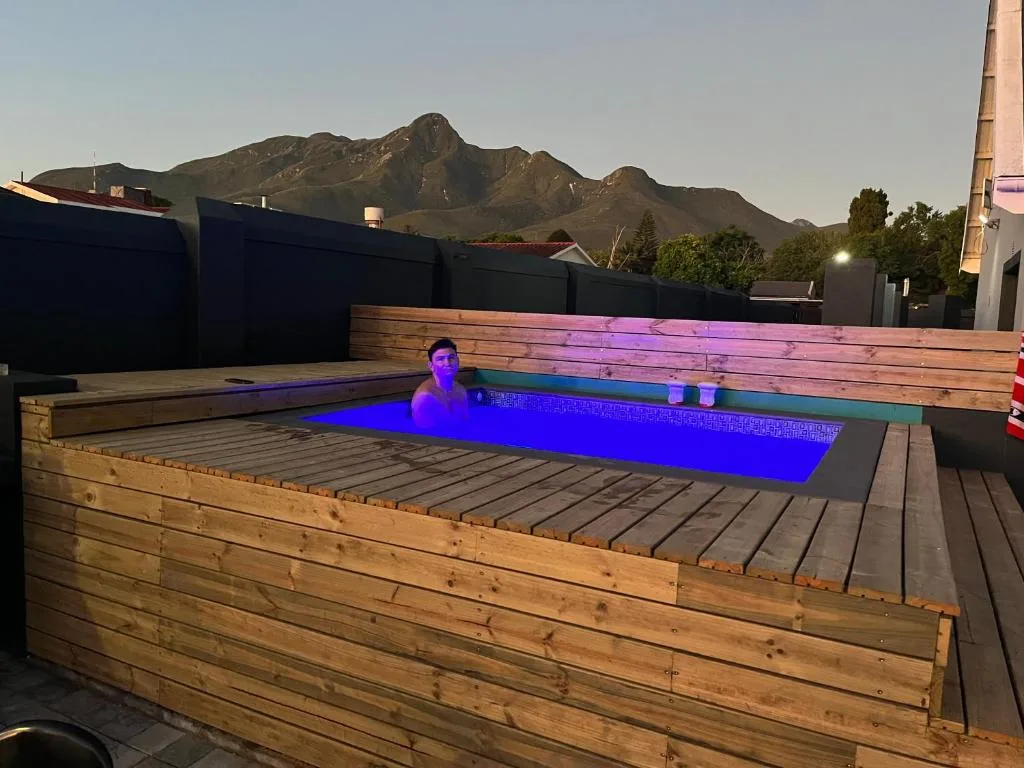 Modern illuminated plunge pool with wooden deck and mountain backdrop at dusk